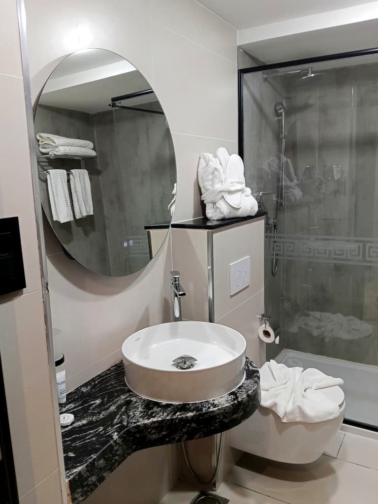 Salle de bain de l'Hôtel Printania avec miroir rond rétroéclairé et vasque sur plan de marbre